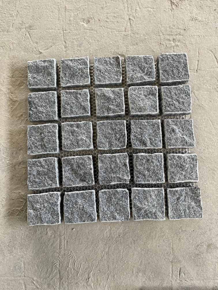 Mesh-mounted granite cobblestones with natural-split faces for patterned outdoor paving.